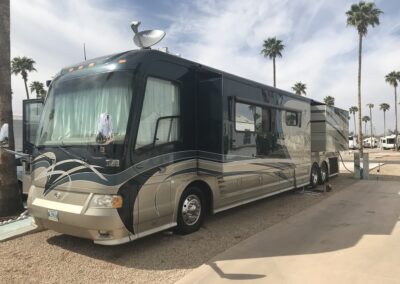 RV parked in lot with palm trees in background.