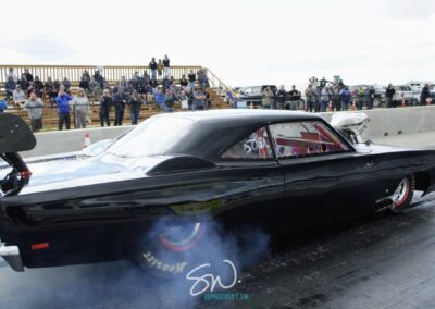 Fast black vehicle accelerating on a drag strip with tire marks visible.