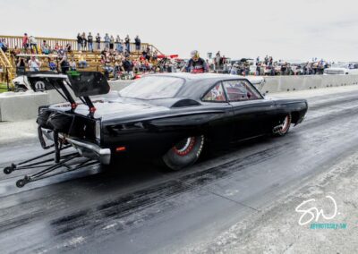 A black car speeding down a drag strip, leaving a trail of smoke behind.