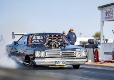 Black sports car racing down a drag strip with blurred background.