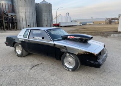 A car parked in front of a grain silo on a sunny day.